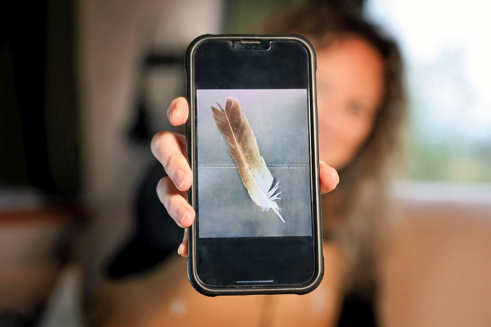 Kristen Kelly holds up a smartphone displaying a photograph of a feather.