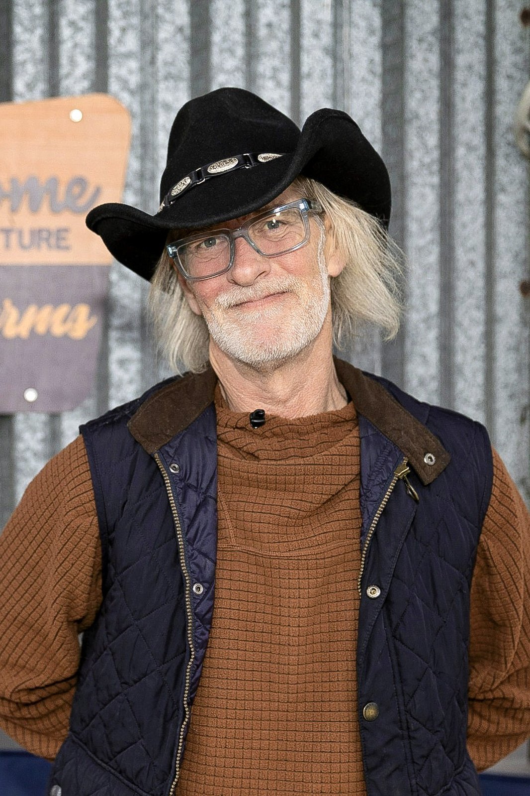 A man in a black cowboy hat and glasses stands smiling in front of a Fancy Lad Farms welcome sign.